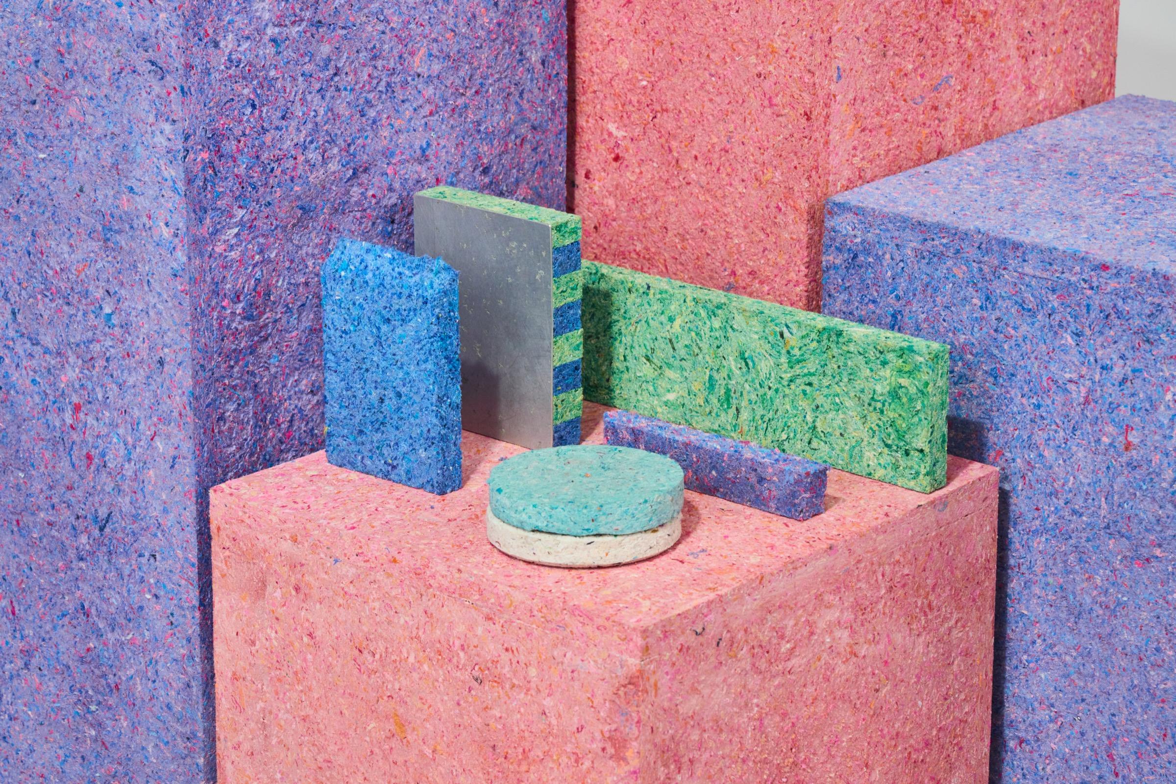 Blocks and panels of recycled fibreboard in pink, lavender, green and blue, stacked into a sculptural arrangement.